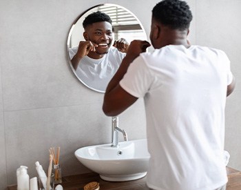 Man smiling while flossing in mirror