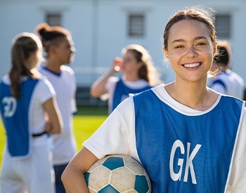 Smiling teen holding soccer ball on field