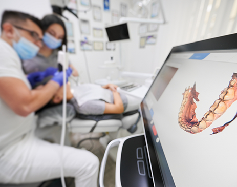 Digital impression on screen in foreground with dentist scanning patient in background