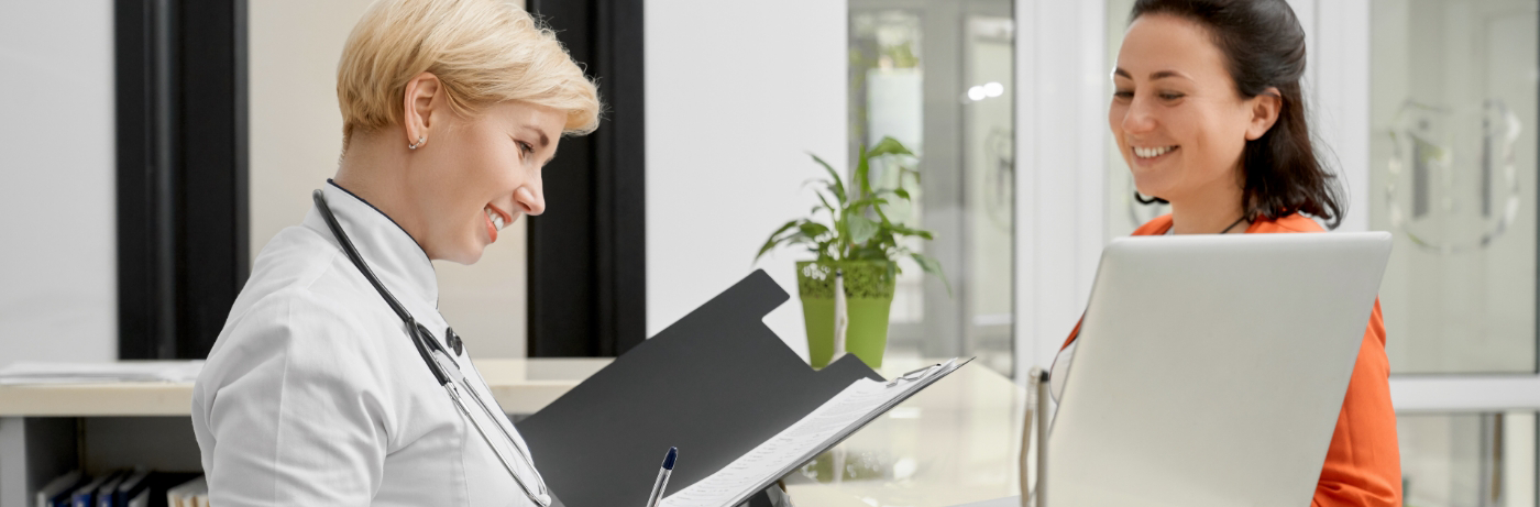 Blonde woman at front desk typing with female patient watching