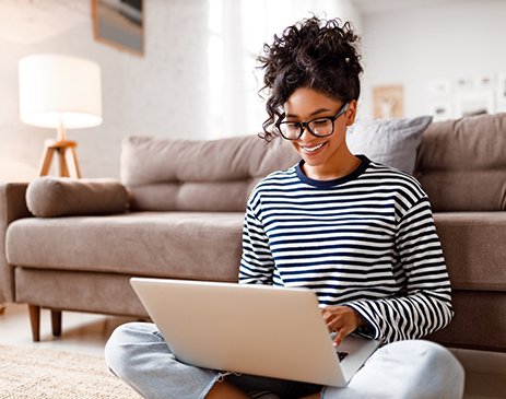 Woman in striped shirt sitting in front of couch with laptop