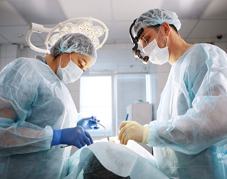 Two masked dentists on either side of patient performing treatment