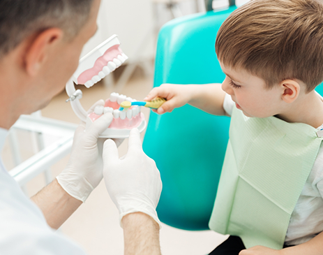 Little boy brushing model teeth held by dentist