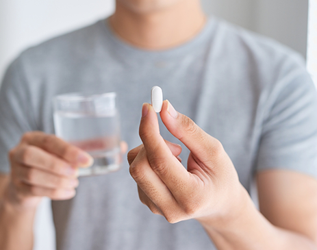 Man in grey shirt holding glass of water and pill