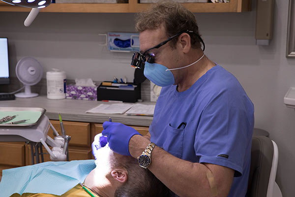 Dr. Harper performing a dental examination on a client laying back in a dental chair at Harper Dental in Fort Smith, AR