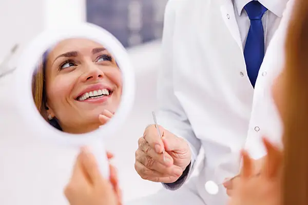 Young woman smiling into mirror with new dental implants at Harper Dental in Fort Smith, AR