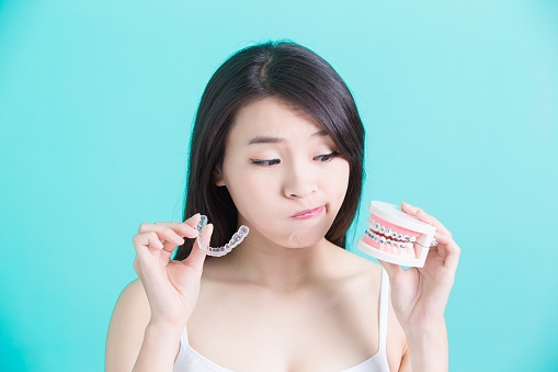 Young woman holding a clear aligner and a 3D model of braces at Harper Dental in Fort Smith, AR