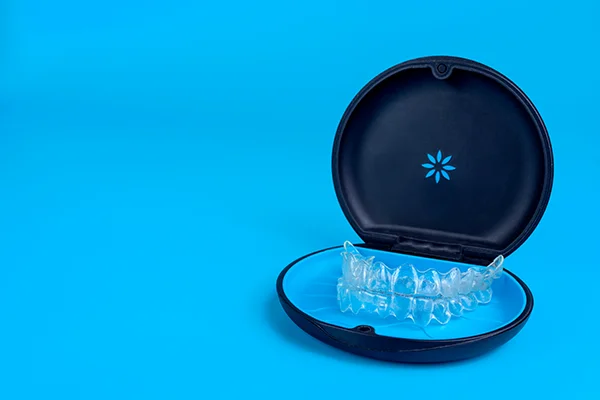 Set of clear aligners resting in an Invisalign® branded case on a blue background at Harper Dental in Fort Smith, AR