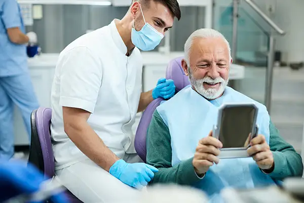 Happy, senior patient looking at himself in a mirror at Harper Dental in Fort Smith, AR